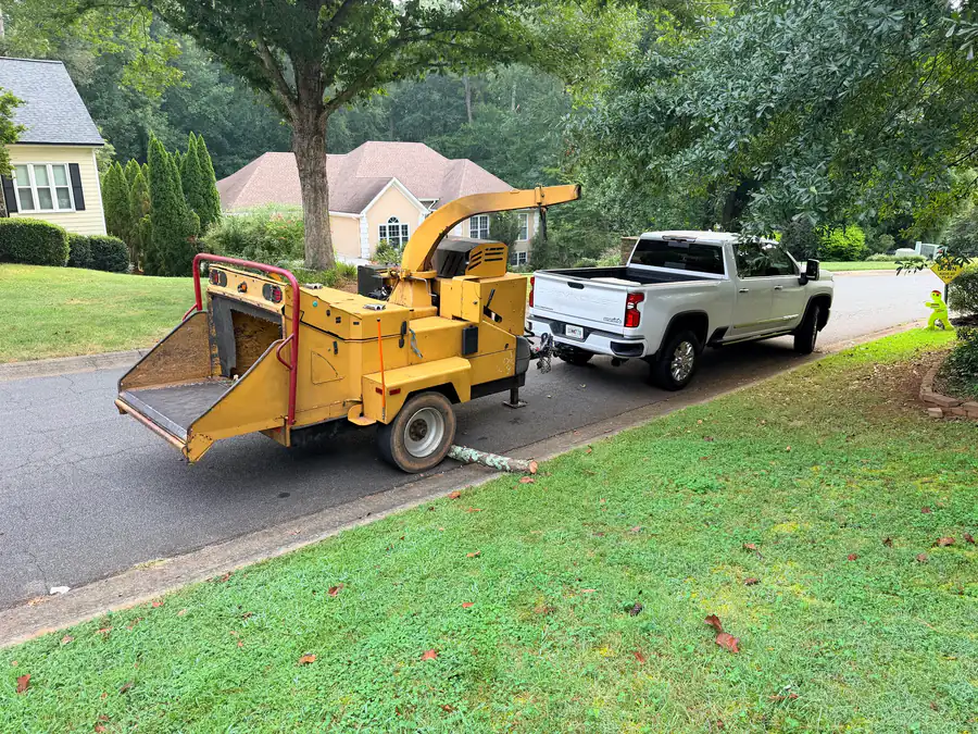 Wood chipper hitched behind a crew truck with fresh-cut logs at the curb